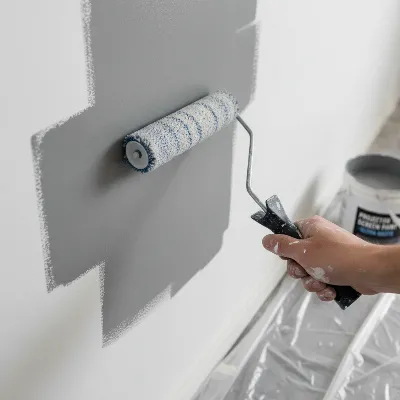 A close-up of a hand applying specialized projector screen paint to a wall with a roller, showing an even, matte finish.